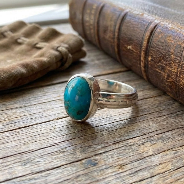 Turquoise ring on a wooden surface with an old book and fabric in the background
